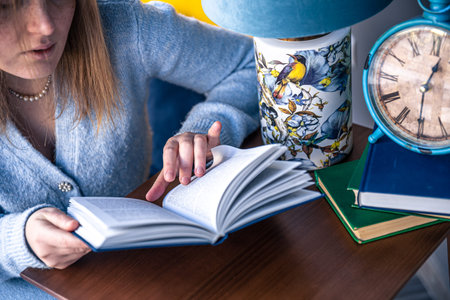 Beautiful young woman is reading a book while sitting at the table.