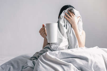A woman holds a cup of coffee while lying in bed.の写真素材