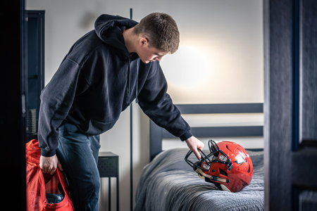 A young man with a football helmet in his room.