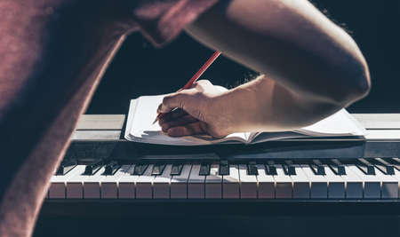 A man plays the piano and writes in a notebook in the dark.の写真素材