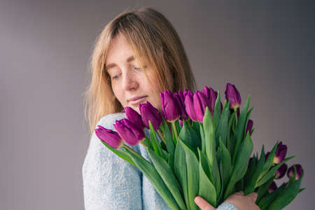 Portrait of a young woman with a bouquet of tulips on a gray background.の写真素材
