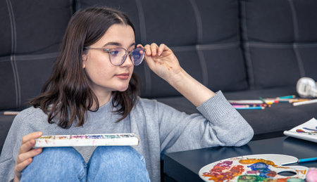 A stylish young woman draws with paints in the home interior.
