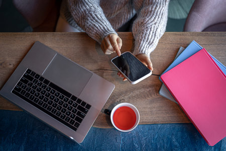 Woman working on a laptop in a cafe with a cup of tea, top view.