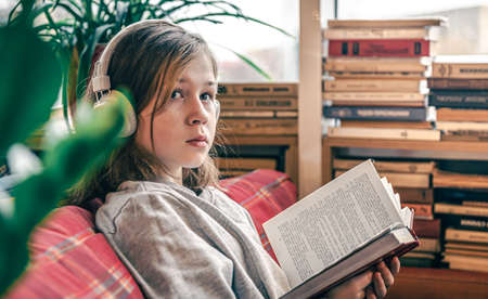 A little girl reads a book and listens to music on headphones.の写真素材