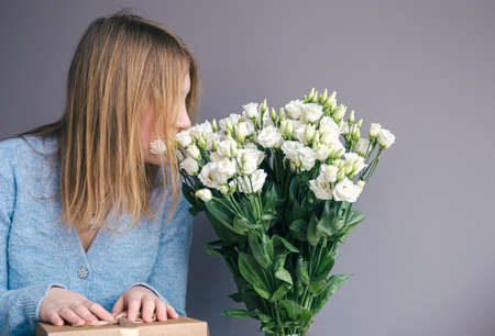 A young woman with a bouquet of roses unpacks a gift box.の写真素材