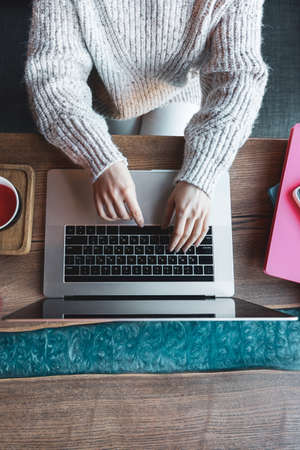 Woman working on a laptop in a cafe with a cup of tea, top view.の写真素材
