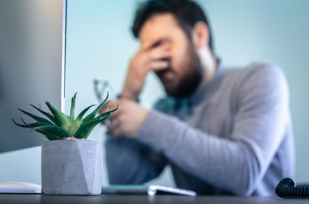 A tired man rubs his eyes in front of a computer screen.の写真素材