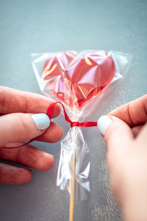Red heart-shaped lollipop in female hands, close up.