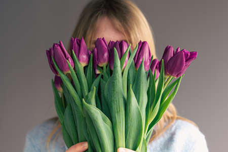 Portrait of a young woman with a bouquet of tulips on a gray background.の写真素材