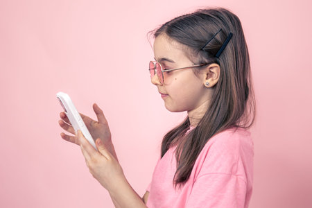 Stylish little girl with a smartphone on a pink background.