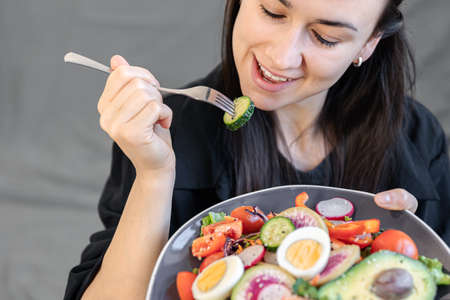 Appetizing salad with fresh vegetables and eggs in a plate in female hands.の写真素材