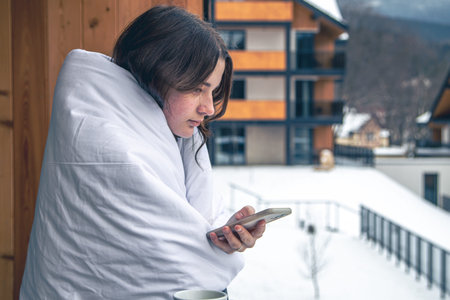 A young woman with smartphone in the mountains on the balcony of the hotel.