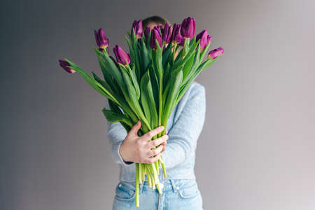 Portrait of a young woman with a bouquet of tulips on a gray background.の写真素材