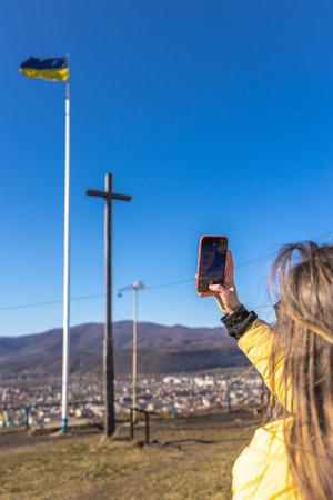 A young woman photographs the flag of Ukraine against the backdrop of the city.