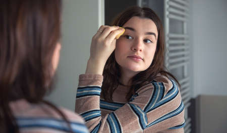 A young woman applies foundation on her face, morning makeup.の写真素材