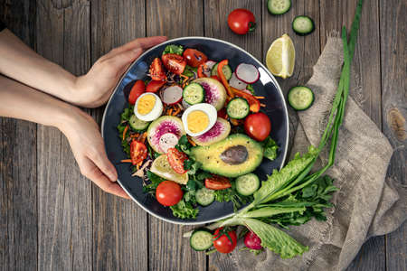 Appetizing vegetable salad with eggs, avocado on a wooden background.の写真素材