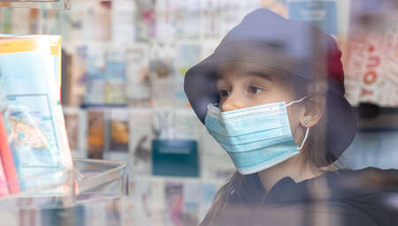 Little girl in a protective medical mask in a bookstore.の写真素材