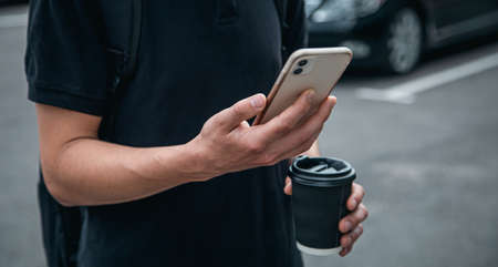 Close-up, smartphone and a glass of coffee in the hands of a man.の写真素材