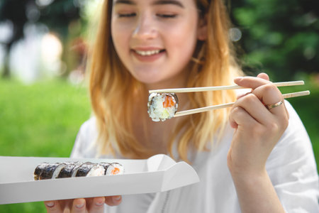 A young woman eating sushi in nature, maki roll close-up.の写真素材