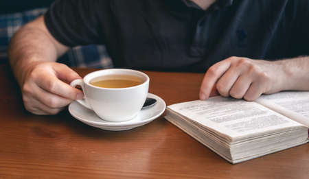 Close-up, a cup of tea and a book in male hands.の写真素材