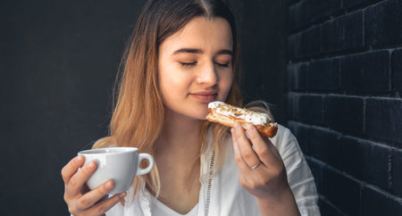 A young woman with a cup of coffee and an eclair in her hands.