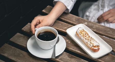 Cup of coffee and eclair on a wooden table close-up.の写真素材