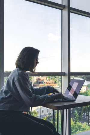 A young woman in glasses works behind a laptop at the workplace.の写真素材