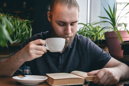 A young man reads a book over a cup of tea in a cafe.の写真素材
