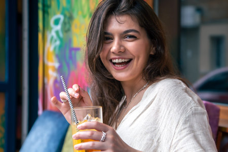 Happy young woman with a glass of lemonade against a bright painted wall.