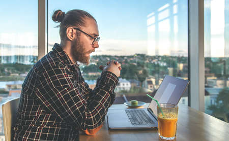 A man with a beard works at a computer, sitting in the office by the window.の写真素材