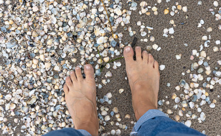 Close-up, female feet on the beach with seashells and sand.