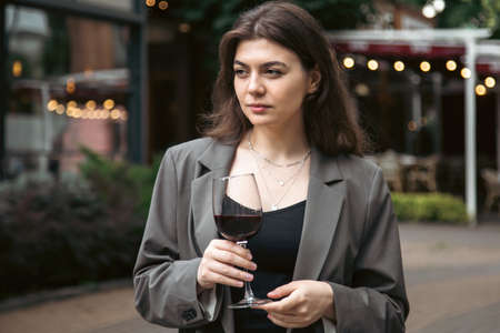 A young woman with a glass of wine outside near a restaurant.の写真素材