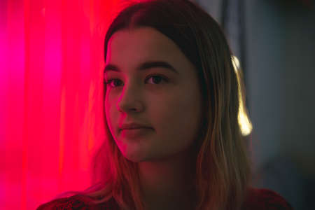 Close up, young womans face in neon red light.の写真素材