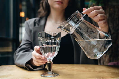 Close-up, a woman pours water into a glass in a cafe.の写真素材