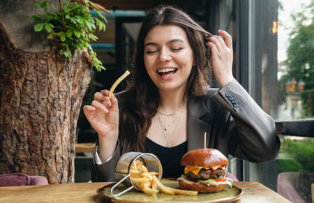 Attractive young woman eating french fries and a burger in a restaurant.の写真素材