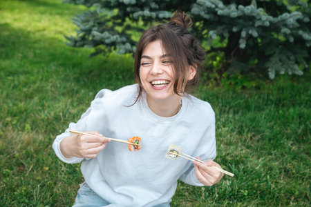 A young woman eating sushi in the park, picnic in nature.
