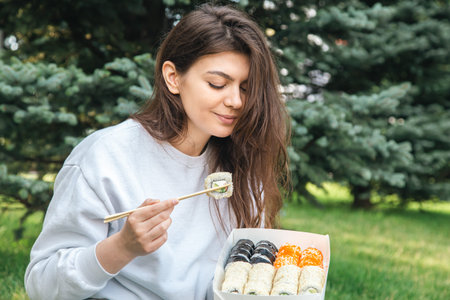 A young woman eating sushi in the park, picnic in nature.