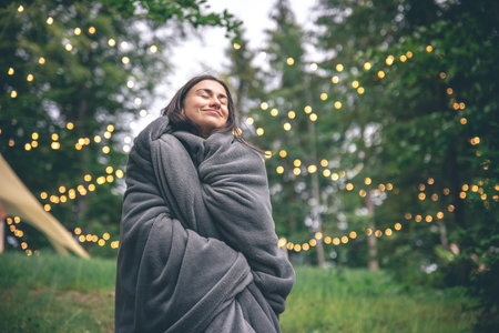 A young woman wrapped in a blanket in the forest on a blurred background.の写真素材