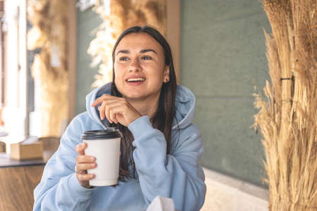 A young woman in a blue hoodie enjoys coffee in the morning in a cafe.の写真素材