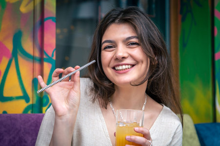 Happy young woman with a glass of lemonade against a bright painted wall.