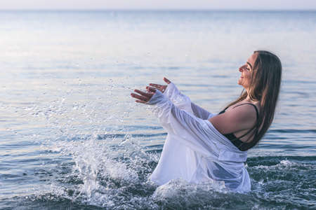 A woman in the sea makes splashes with water.の写真素材