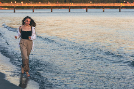 A woman walks along the sea barefoot at sunset, copy space.