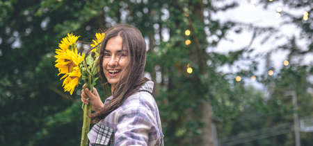 A young woman with a bouquet of sunflowers on a blurred background in nature.の写真素材