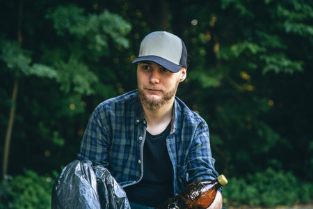 A young man with a trash bag in the forest cleans up plastic bottles.