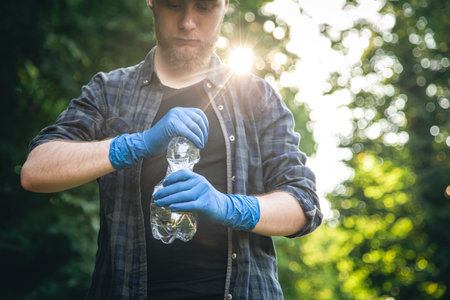 A man in gloves with a plastic bottle in his hands cleans the forest.