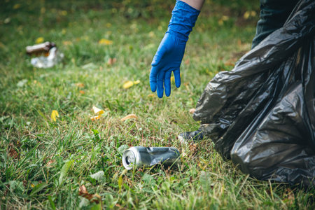 A mans hand in a glove cleans up garbage in the forest.