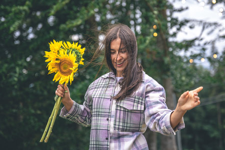 A young woman with a bouquet of sunflowers on a blurred background in nature.