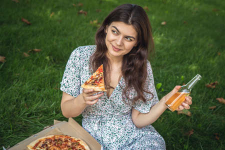 Happy young woman eating pizza at a picnic.の写真素材