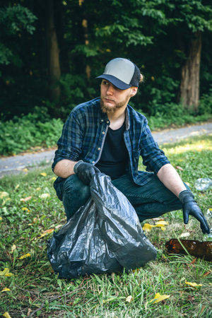 A young man with a trash bag in the forest cleans up plastic bottles.