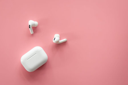 Wireless in-ear headphones with a case on a pink background, flat lay.